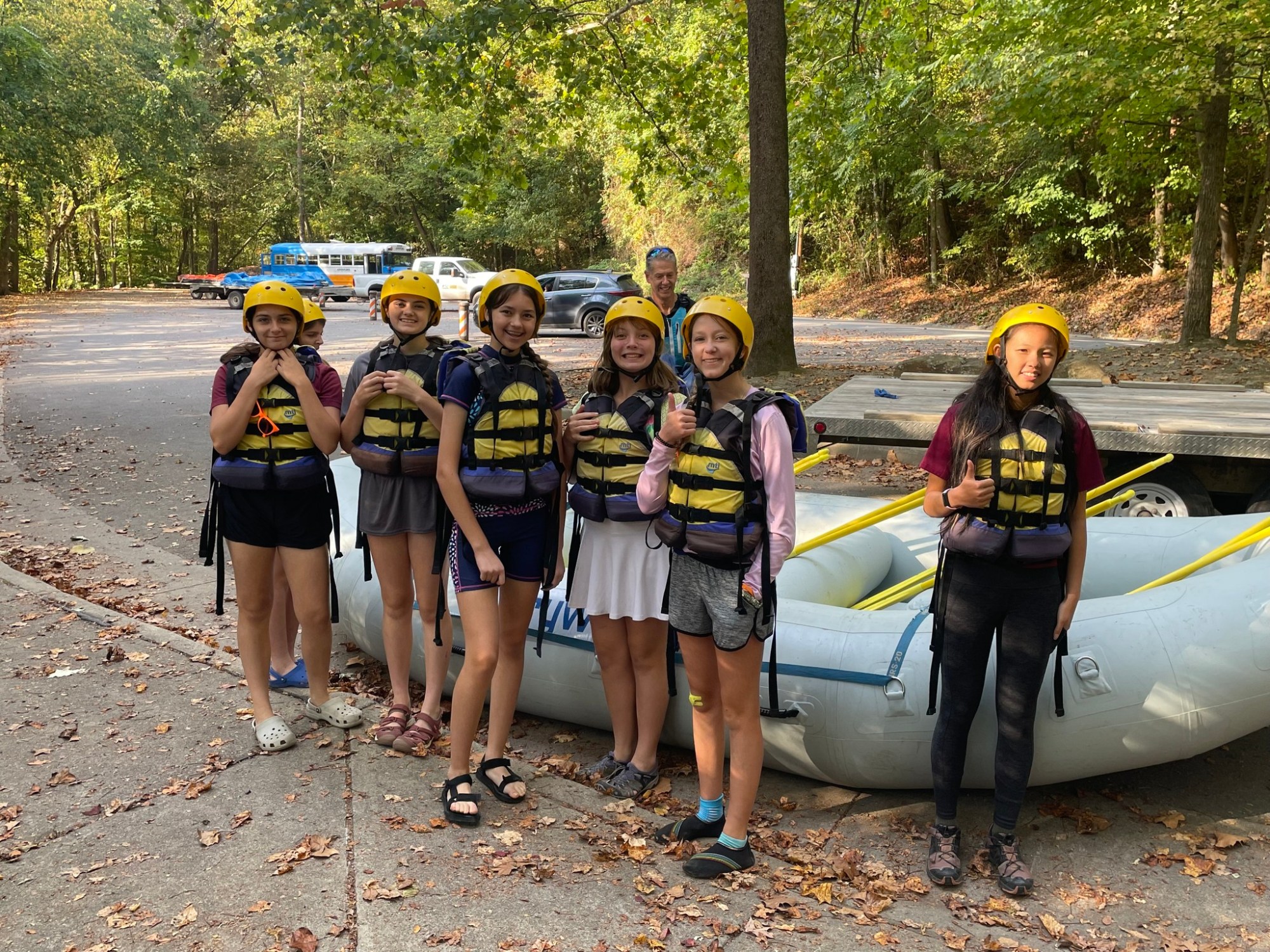 Seven people in helmets and life jackets standing by an inflatable raft in a wooded area.