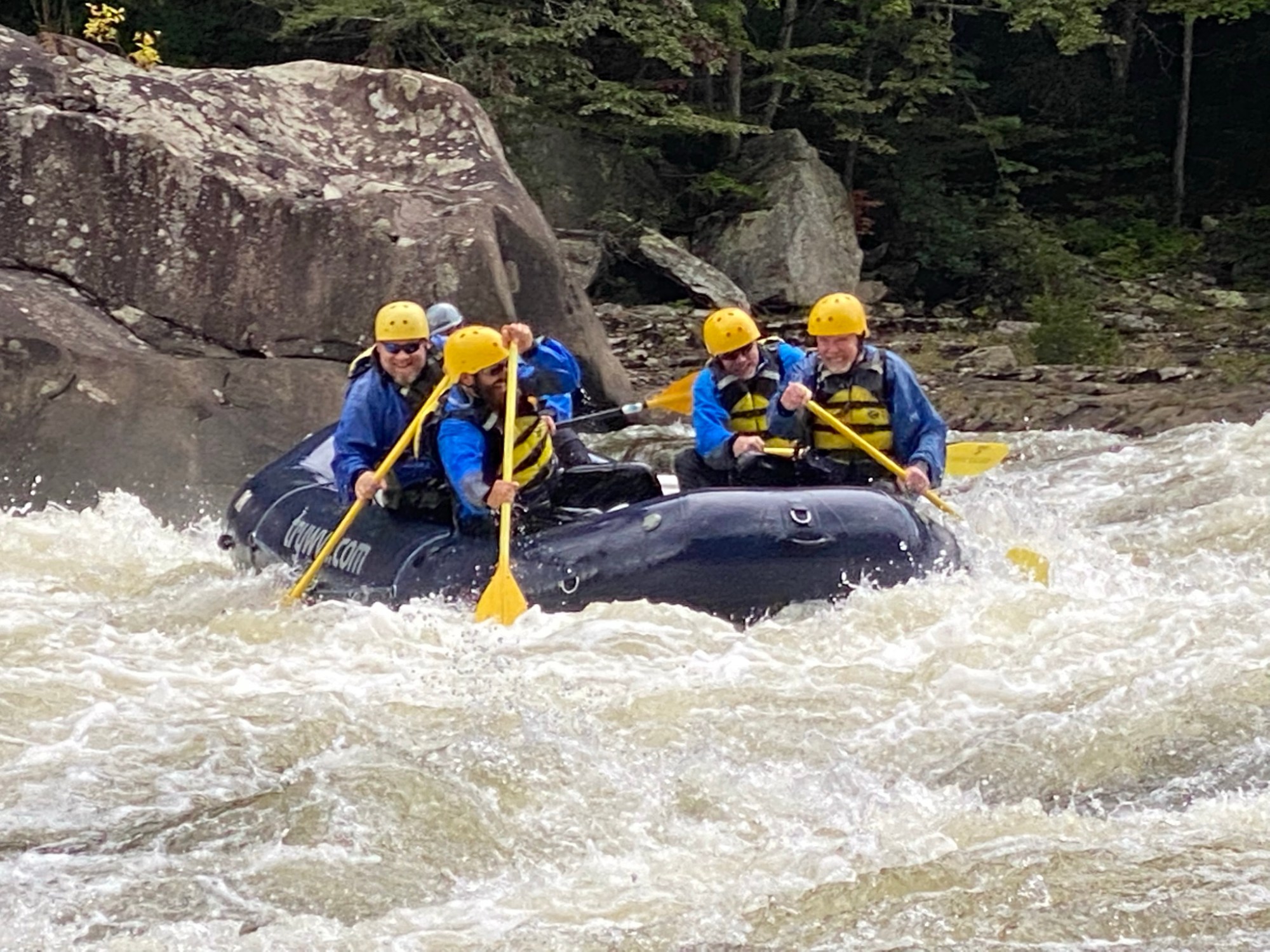 Group of people whitewater rafting with helmets and paddles in a turbulent river.