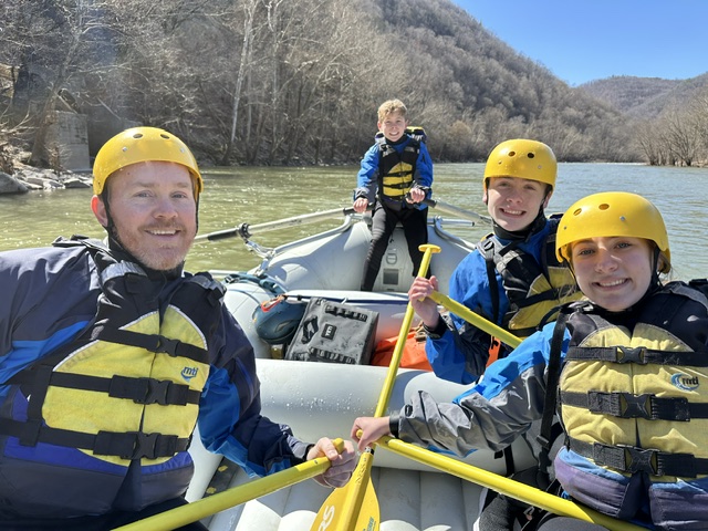 Four people in helmets and life vests rafting on a river.