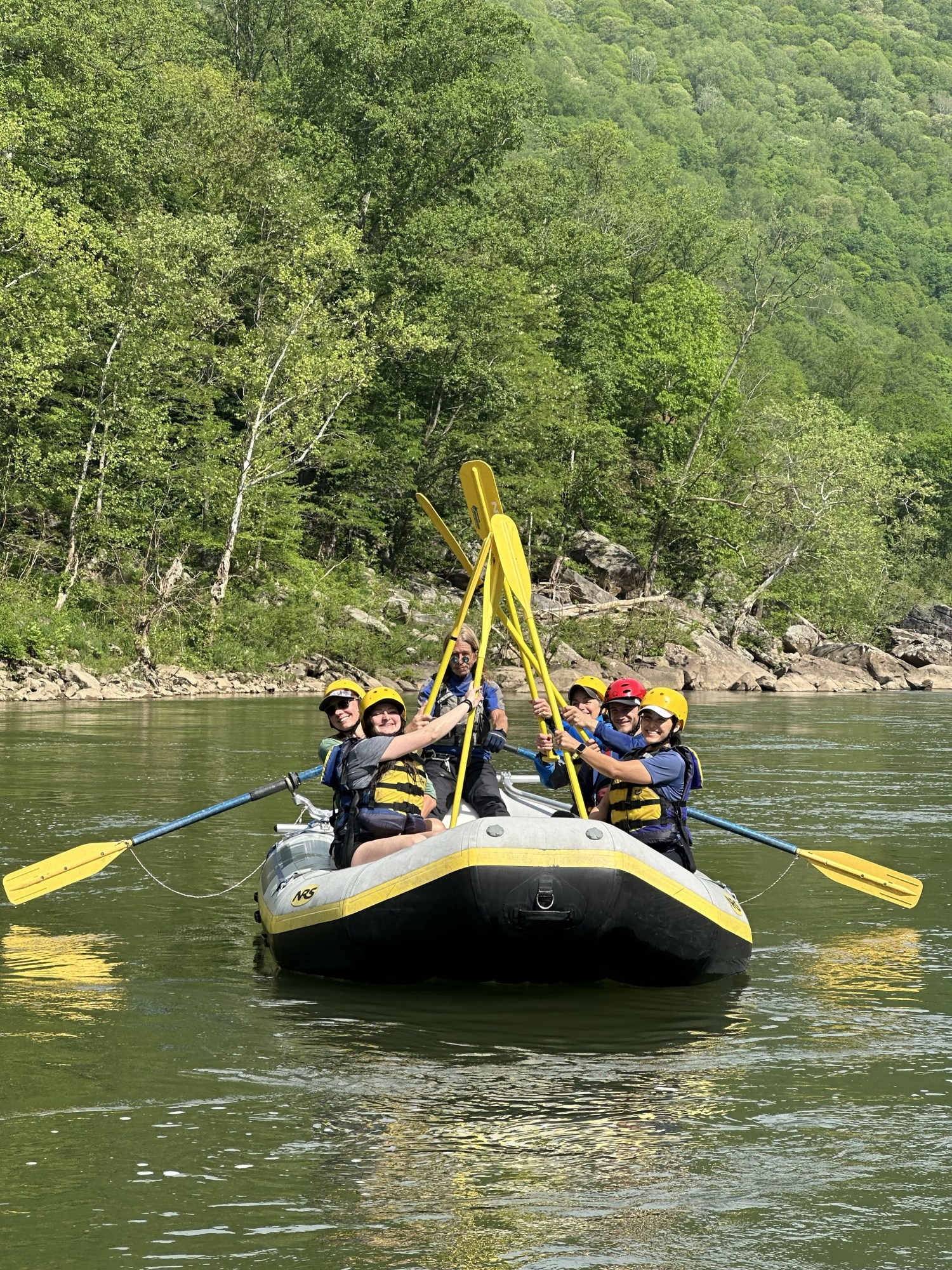 Group of people rafting on a river, holding paddles together, surrounded by lush green forest.