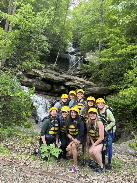 Group of people in helmets and vests pose in front of a waterfall surrounded by lush greenery.