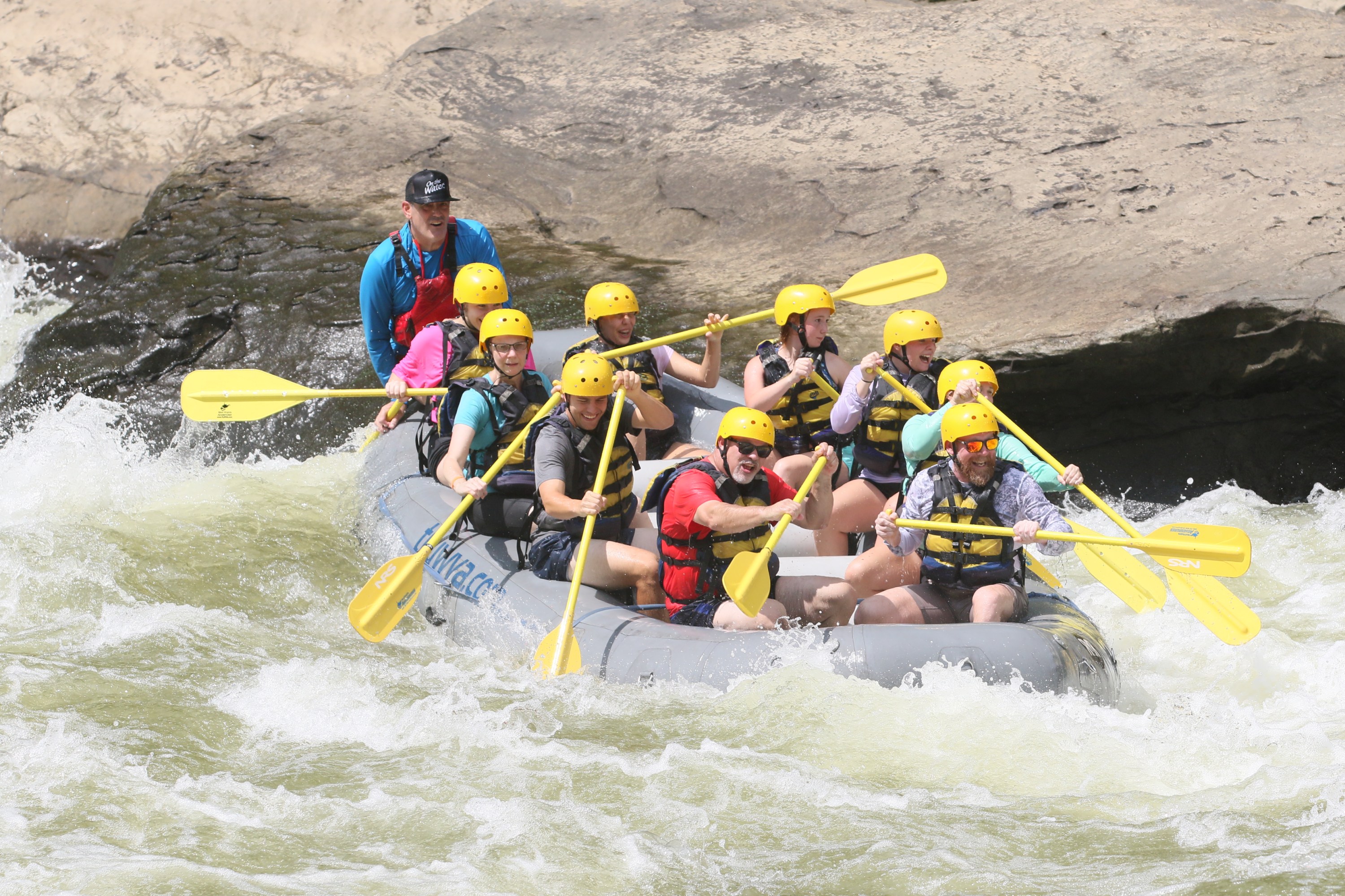 Group of people white-water rafting with yellow paddles and helmets.