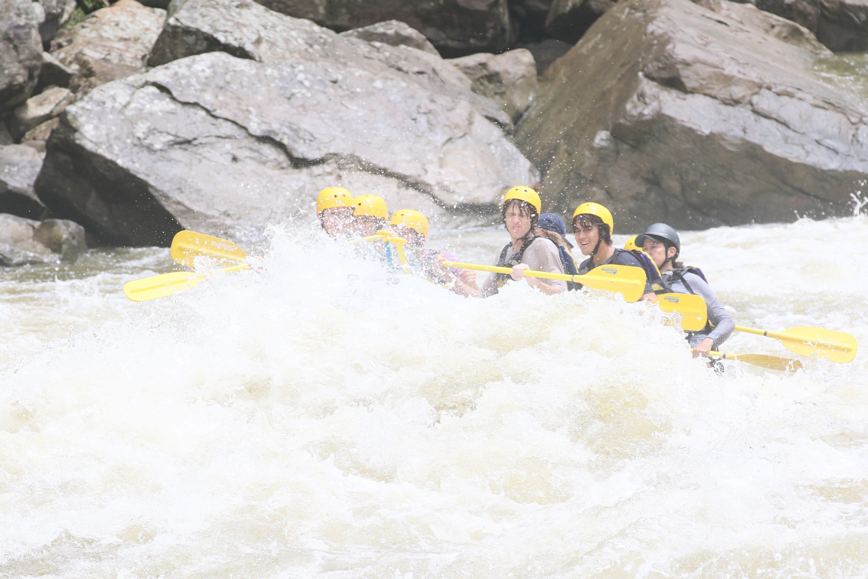 People in yellow helmets whitewater rafting in a rocky river.