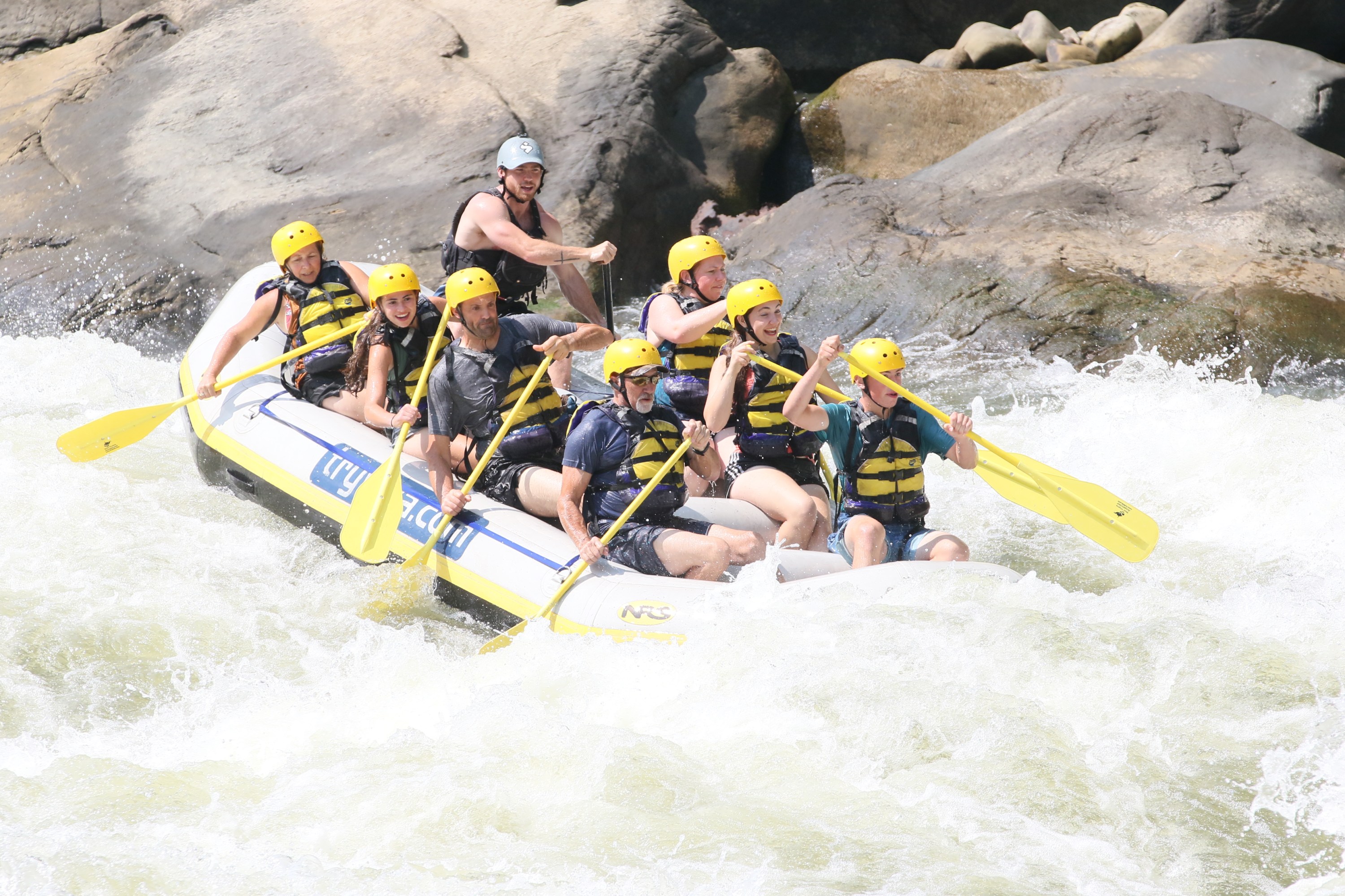 Group whitewater rafting in rough river, wearing helmets and life vests.