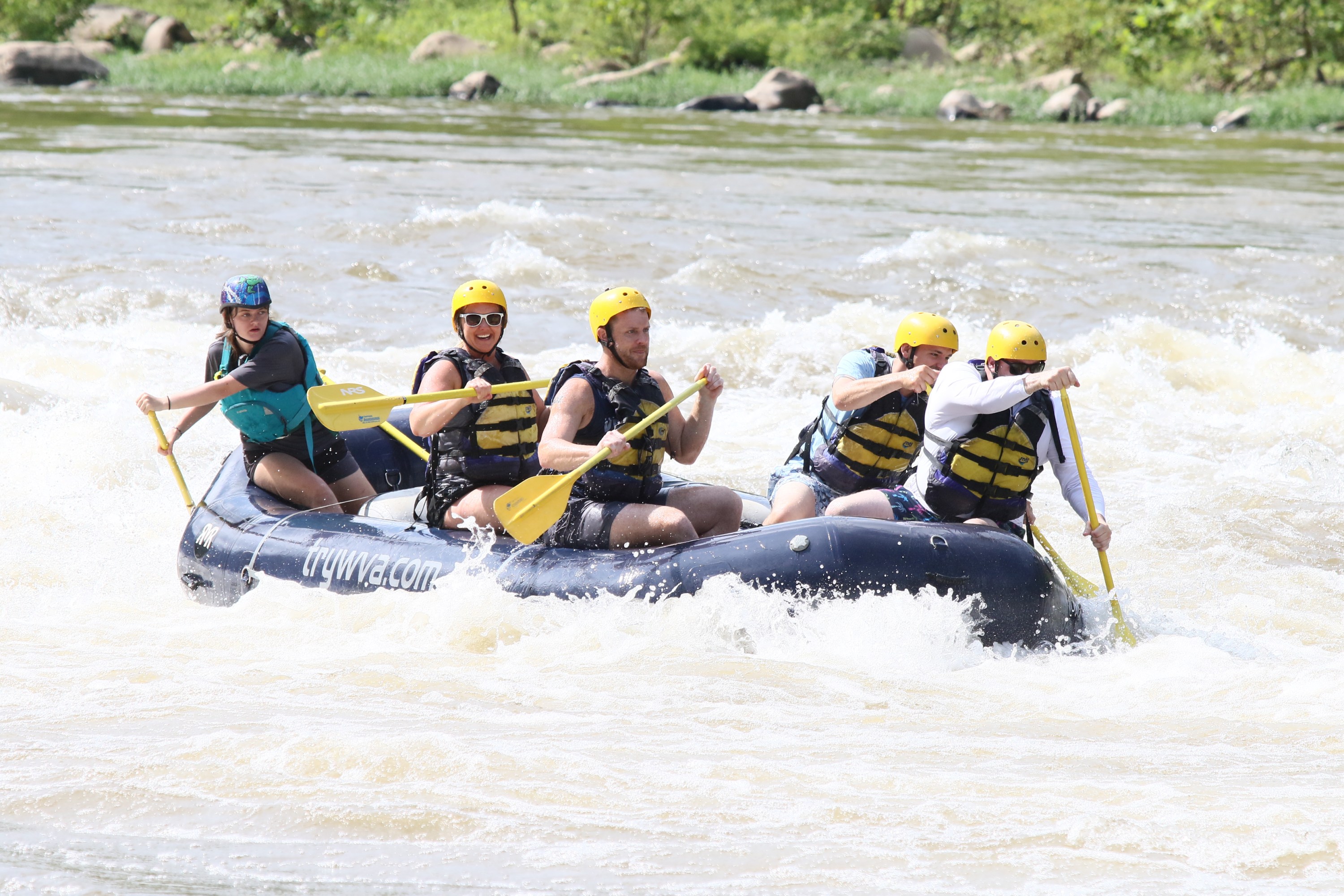 Group of people rafting on a river, wearing helmets and life jackets.
