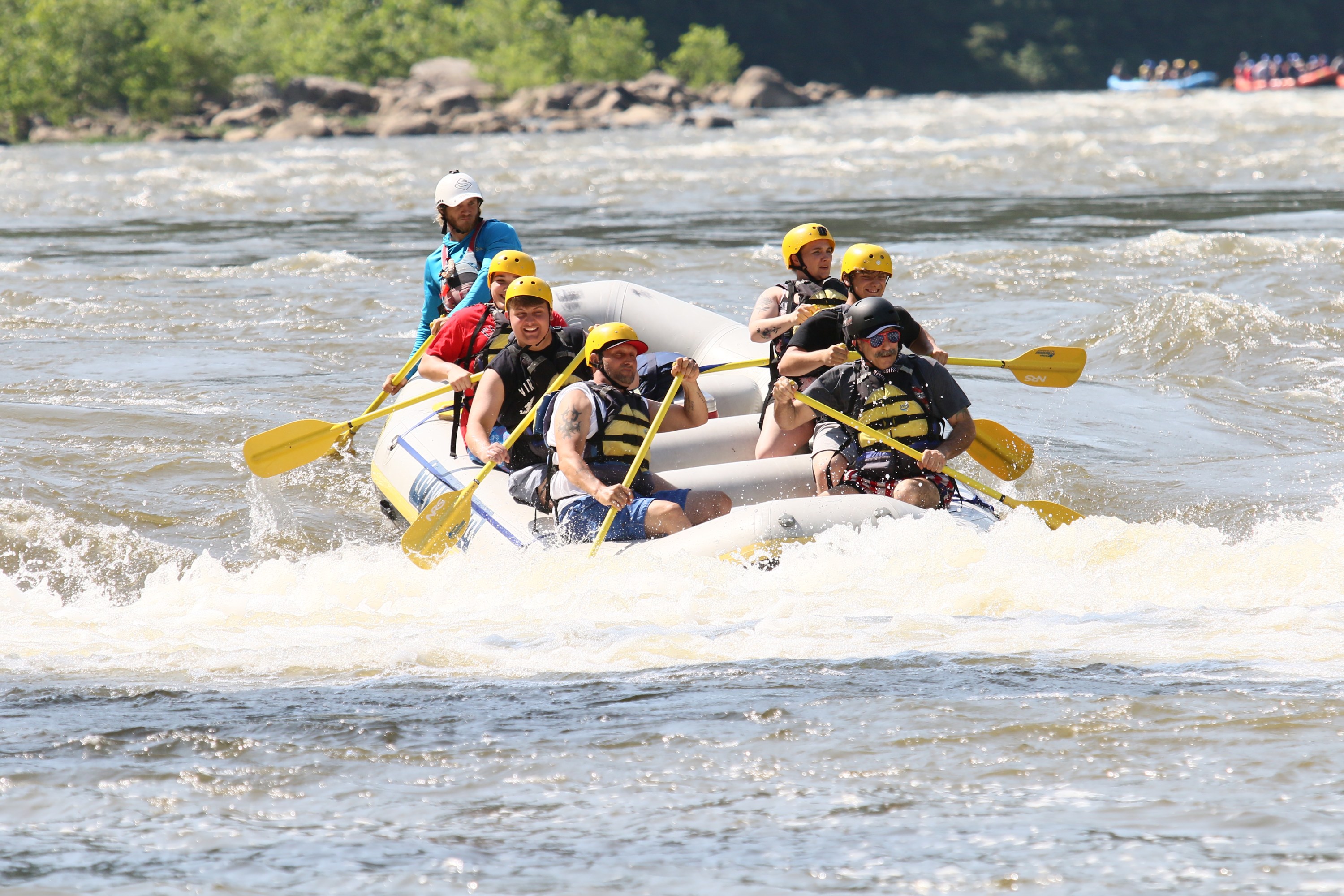 Group rafting on a river; wearing helmets and vests.