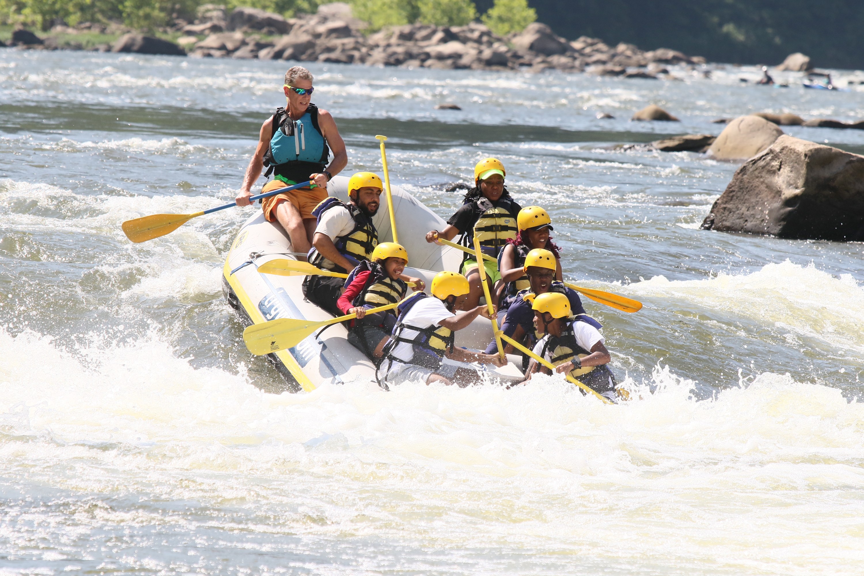 Group of people whitewater rafting on a river, wearing helmets and life vests.