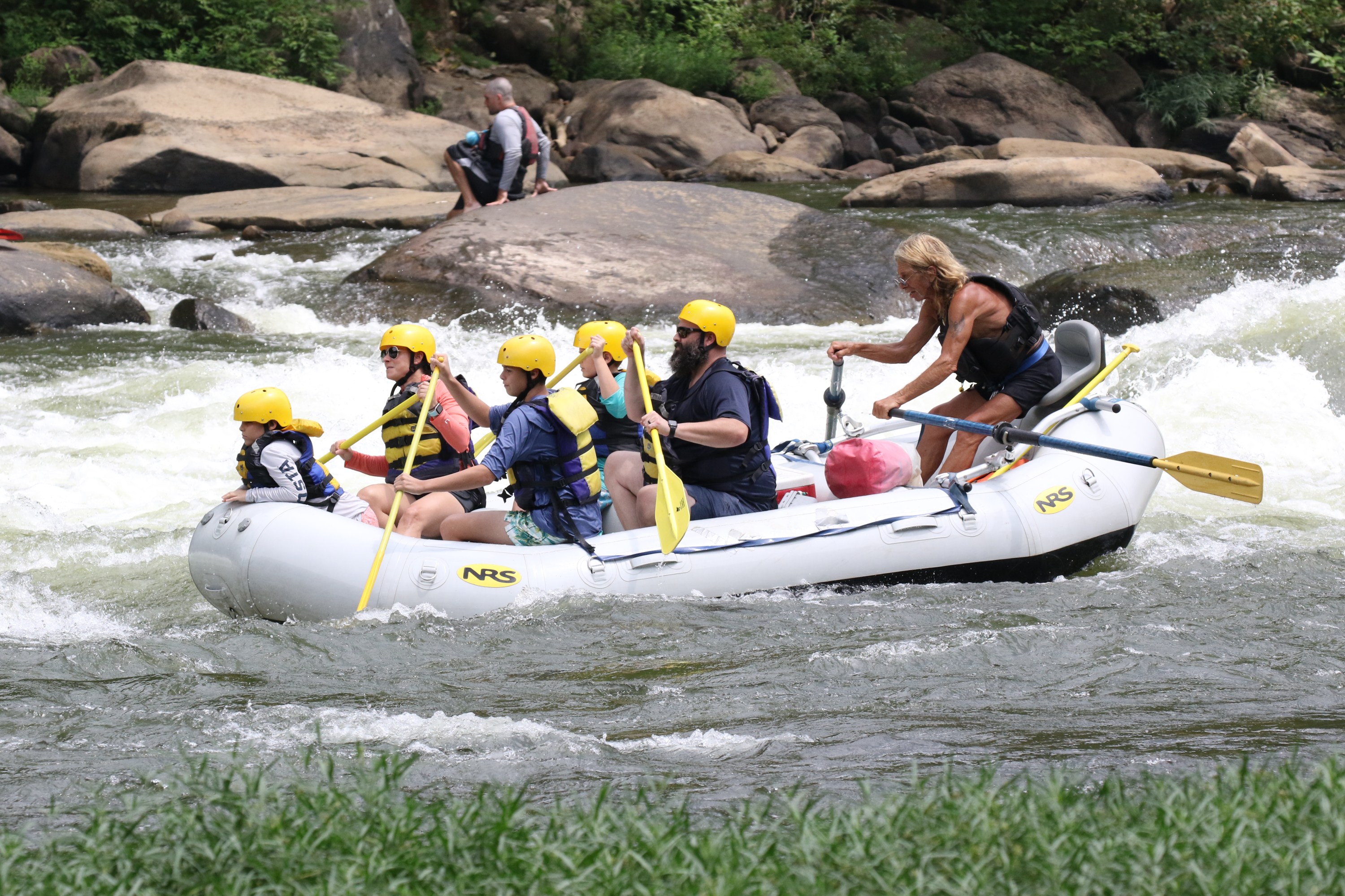 Group white-water rafting on a river, wearing helmets and life jackets.