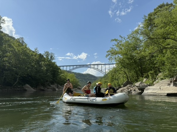 Group rafting on a river with a bridge in the background on a sunny day.