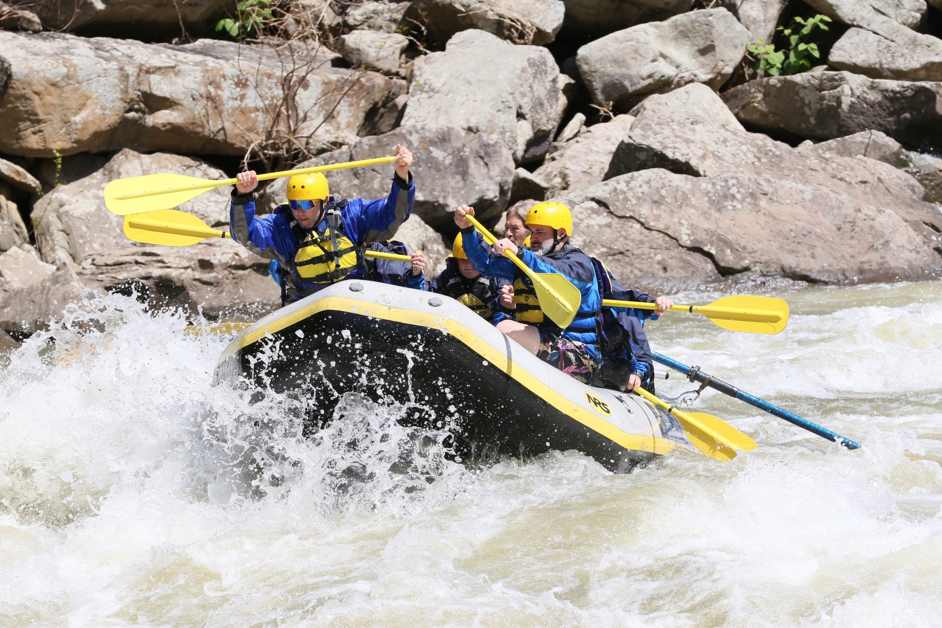 Four people in helmets rafting through whitewater rapids.