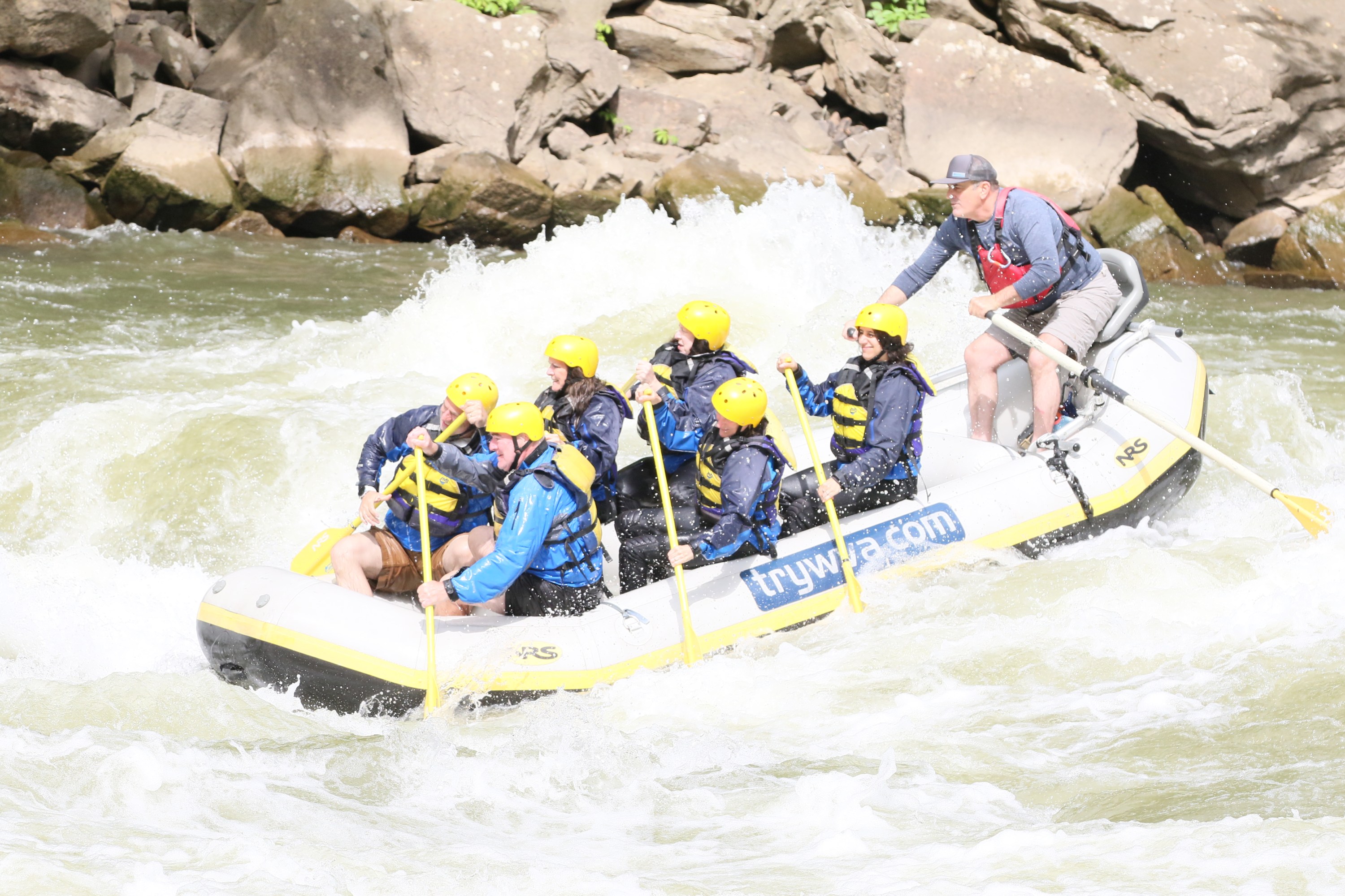 Group whitewater rafting with helmets and paddles in turbulent river.