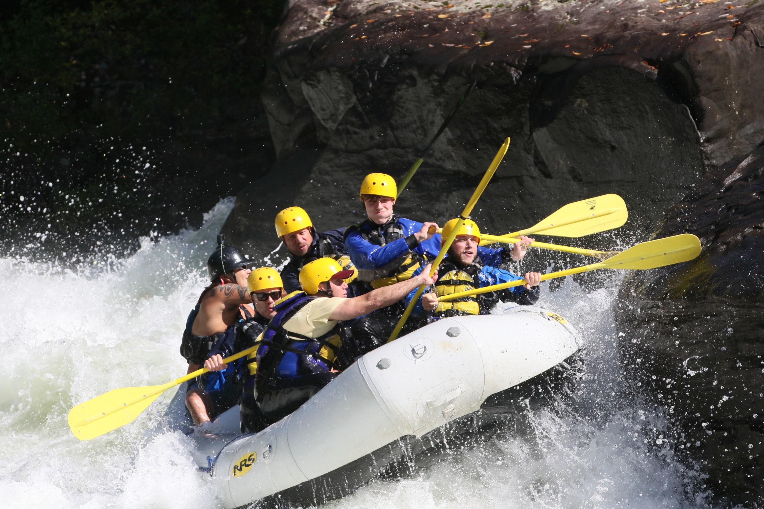 Group of people whitewater rafting with helmets and paddles in a rapid.