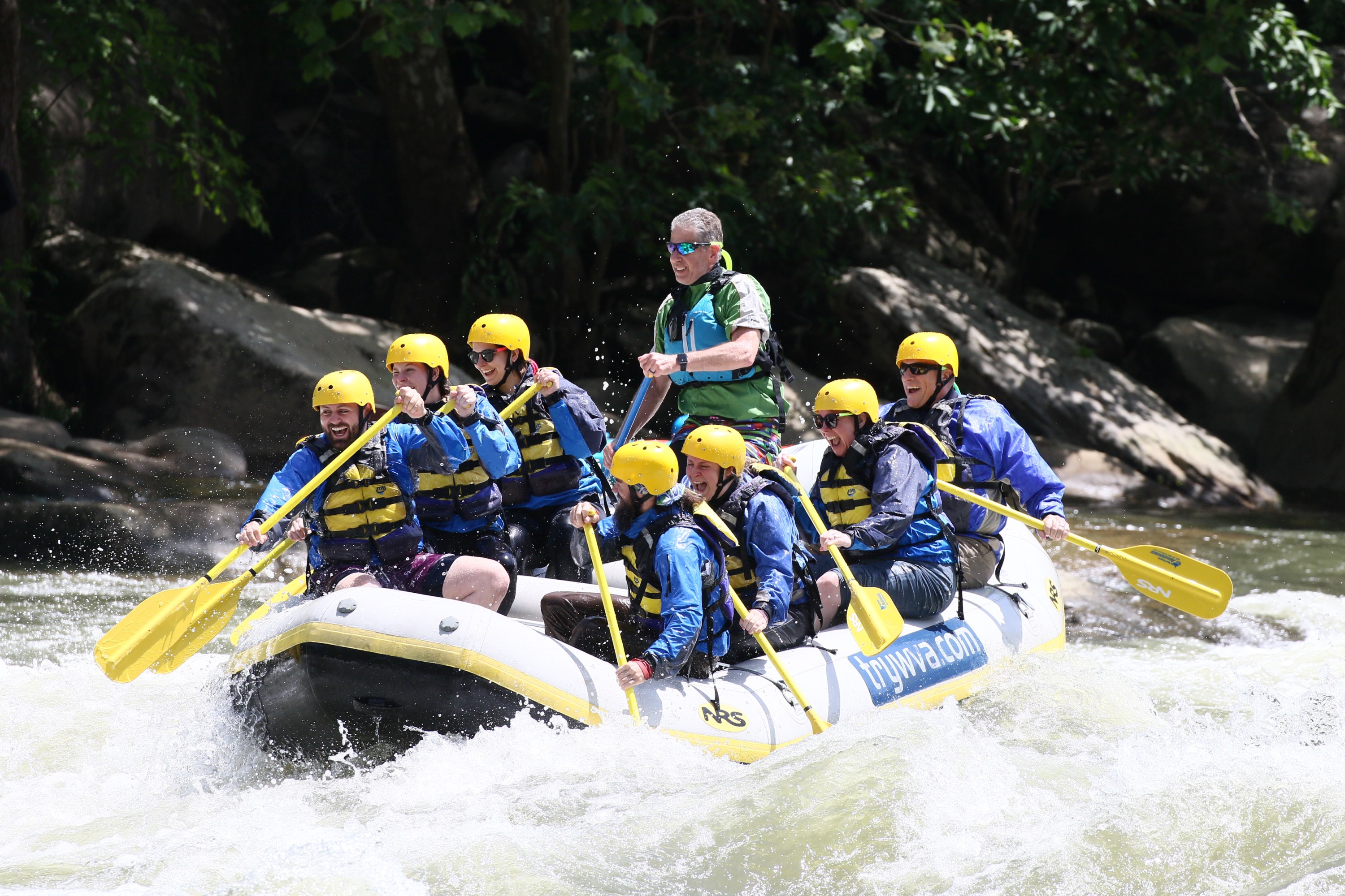 Group rafting on a river with yellow helmets and paddles.