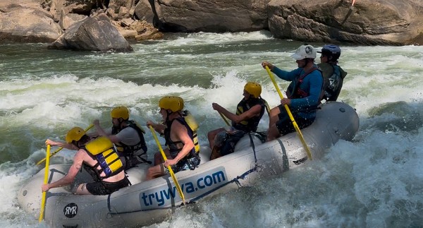 Group rafting on whitewater river in inflatable boat with paddles.