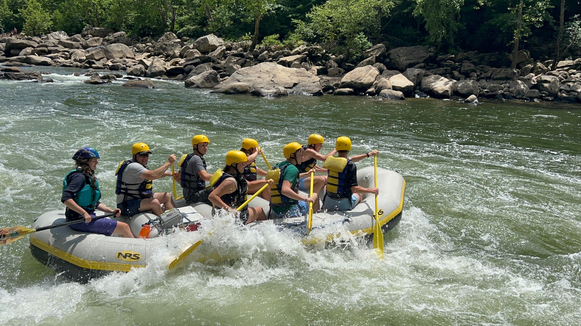 Group white-water rafting on a river with helmets and life jackets.