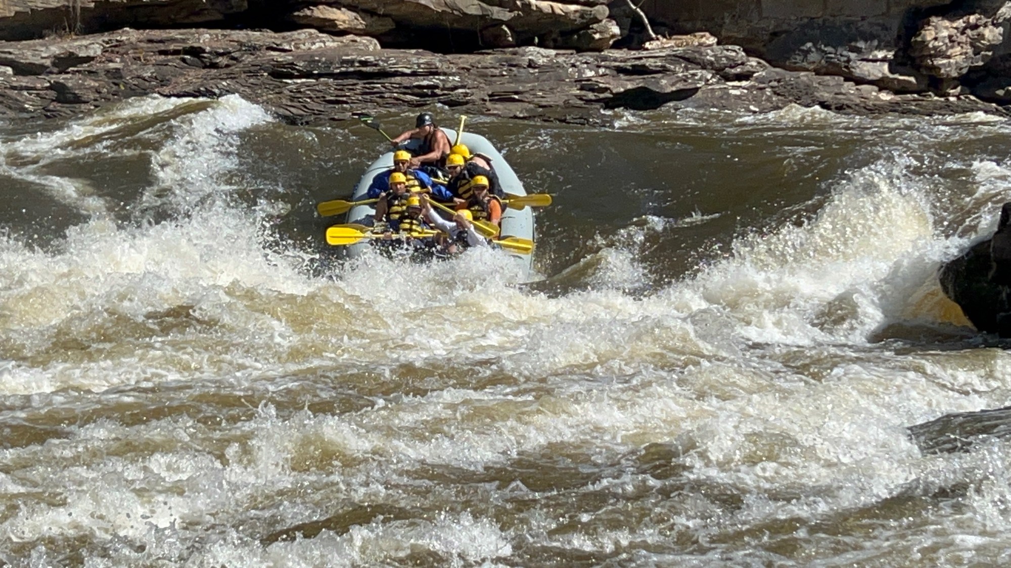 Group whitewater rafting on a turbulent river with rocky banks.