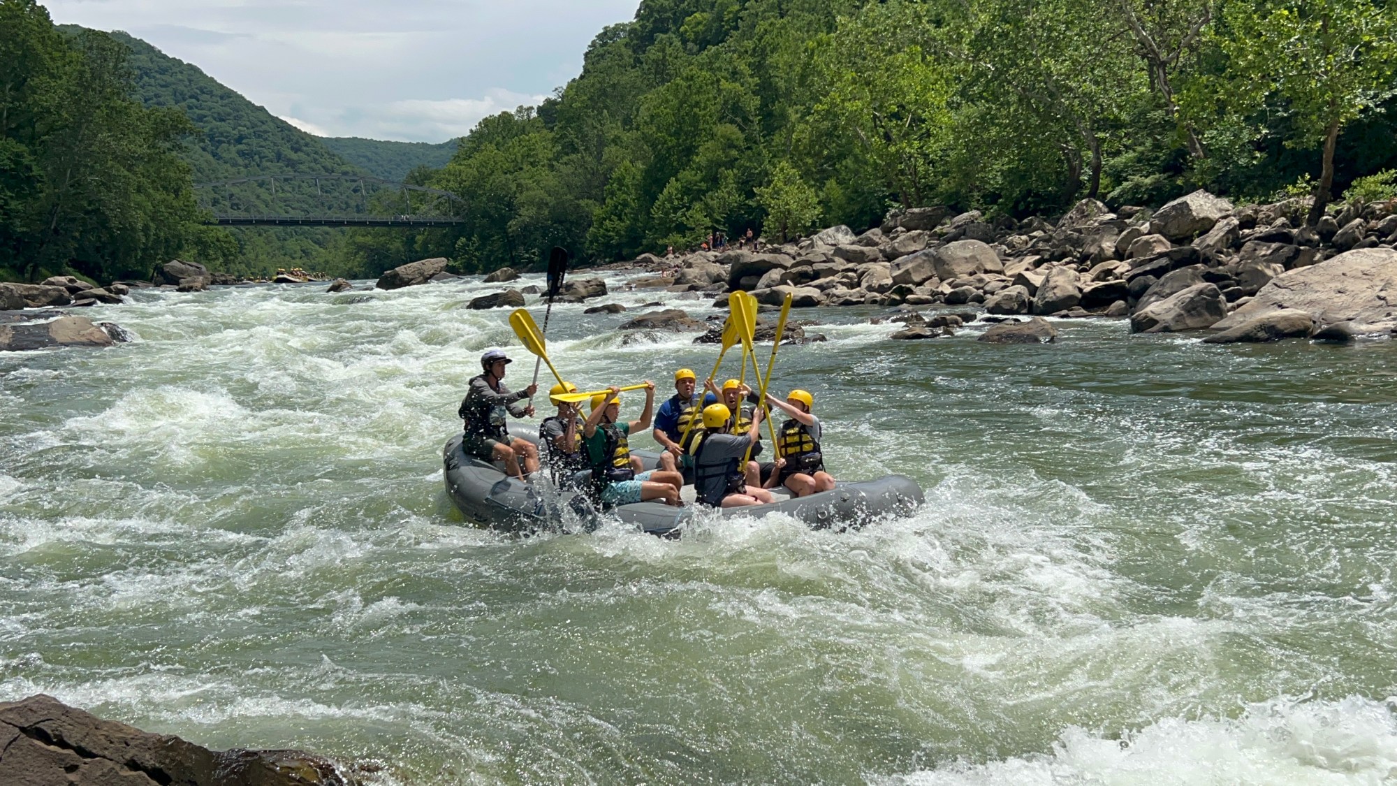Group whitewater rafting on a river surrounded by trees and rocks.
