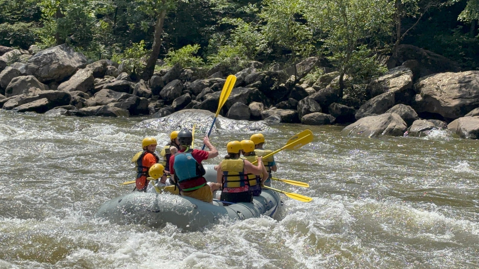 Group white water rafting with yellow helmets and paddles in a river.