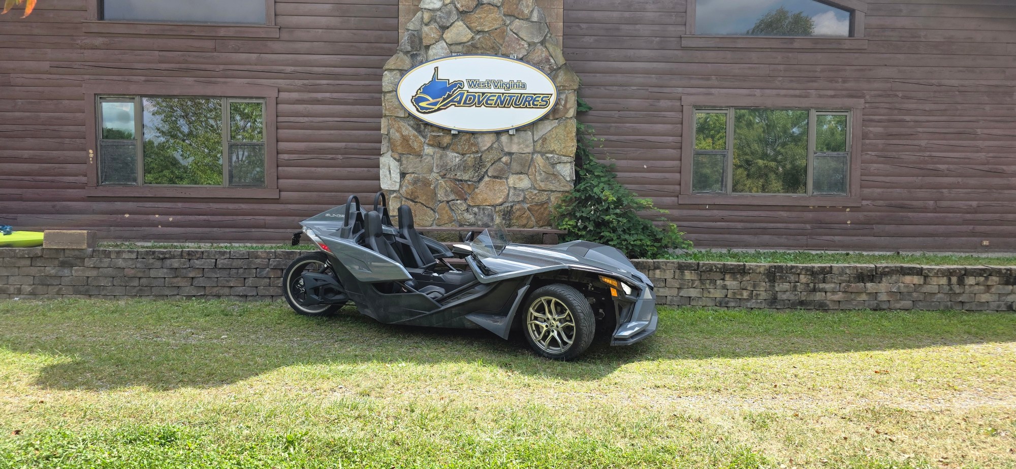 A three-wheeled vehicle parked on grass in front of a wooden building.