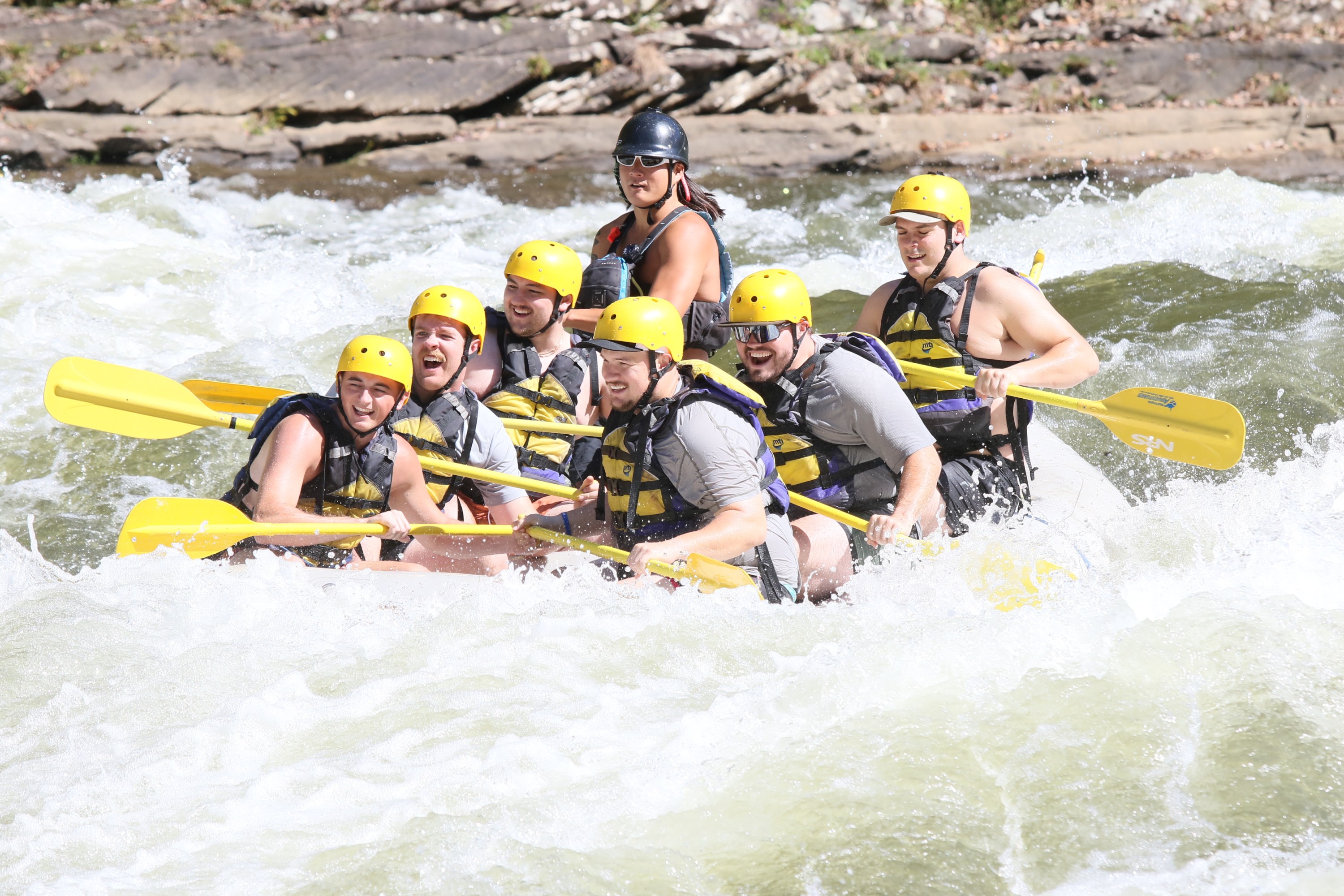 Group of people white-water rafting, wearing helmets and life jackets.