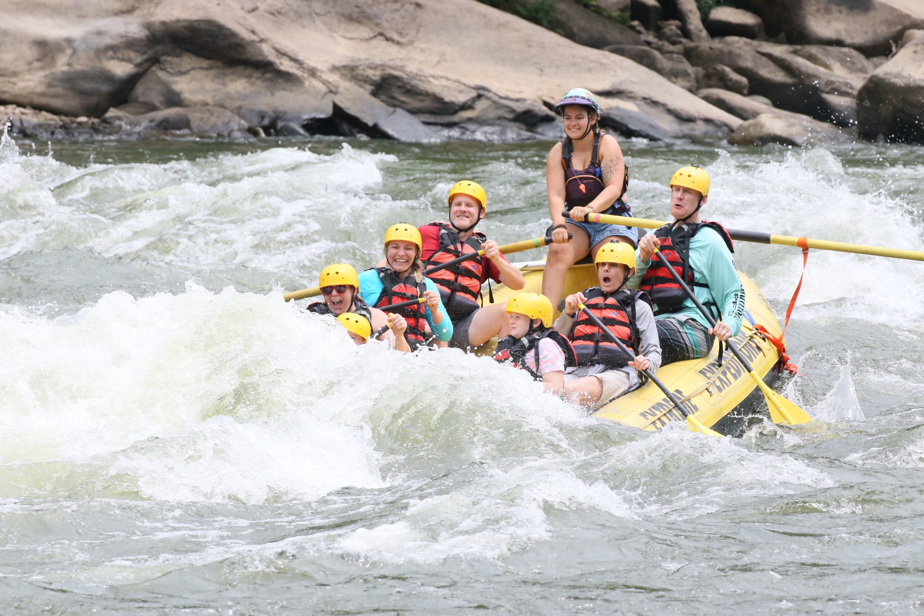Group rafting on a river with helmets and life vests.