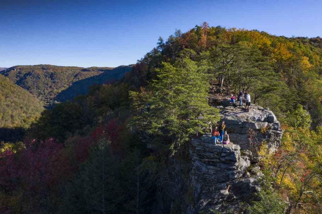 People on a rocky outcrop with trees overlooking a forested valley.