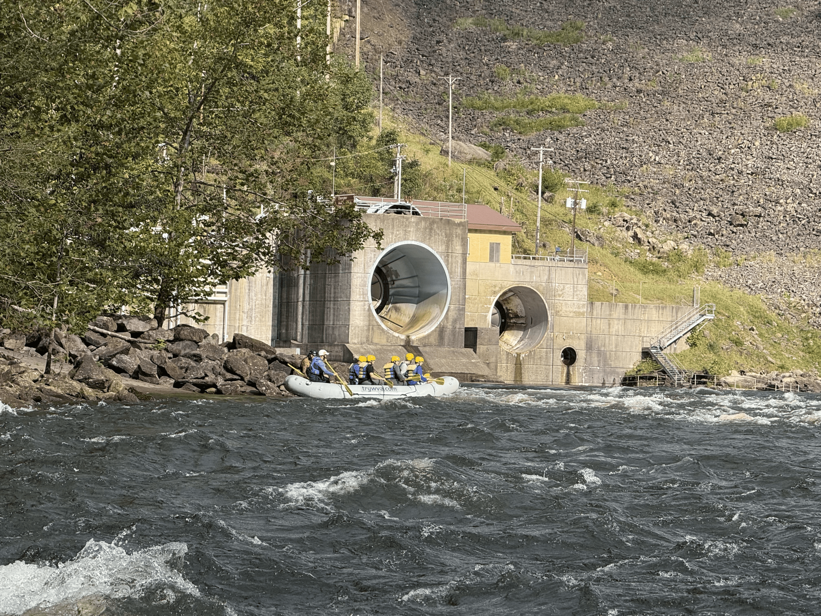 Rafters in a white raft approaching dam outlet on a rocky river.