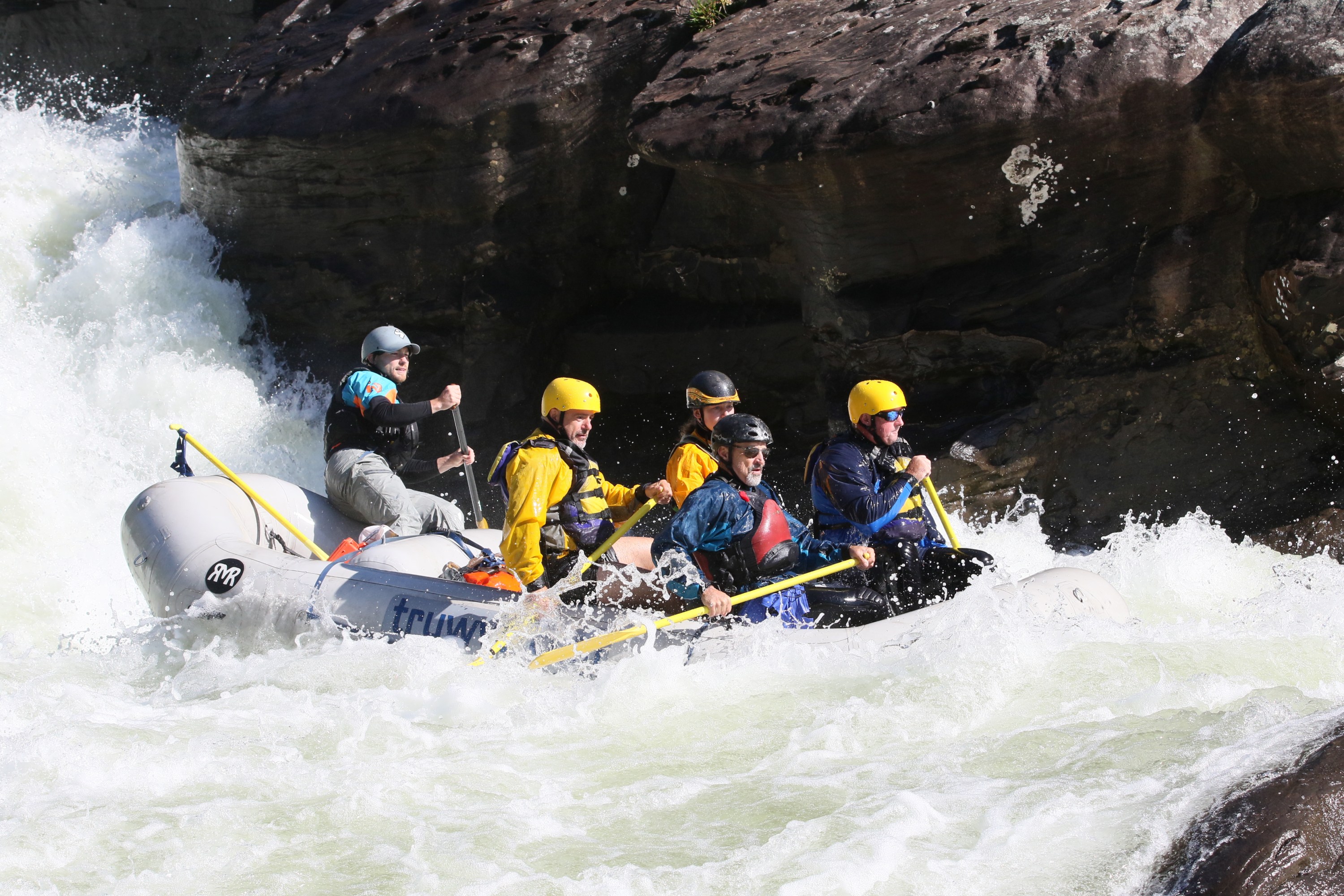 Group of people in helmets rafting on rough river rapids.
