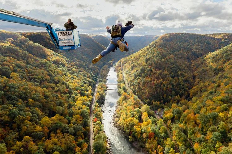 Person BASE jumping off platform above a forested valley with river below.