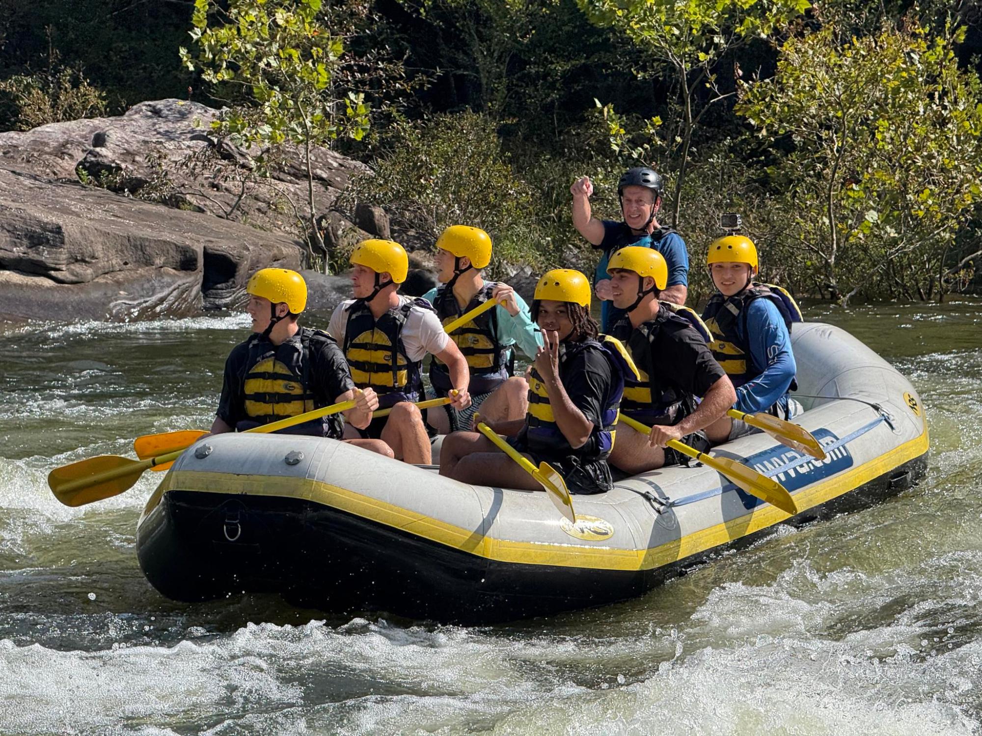 Group whitewater rafting in a blue raft wearing yellow helmets and life jackets.